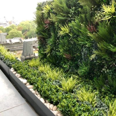 Artificial plants in front of living wall with pebble border