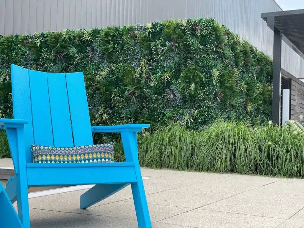A vibrant blue chair sits on a patio next to a green wall reminiscent of the lush installations seen in fitness centers across Houston, Texas. A patterned cushion graces the chair, surrounded by sleek modern architectural elements.