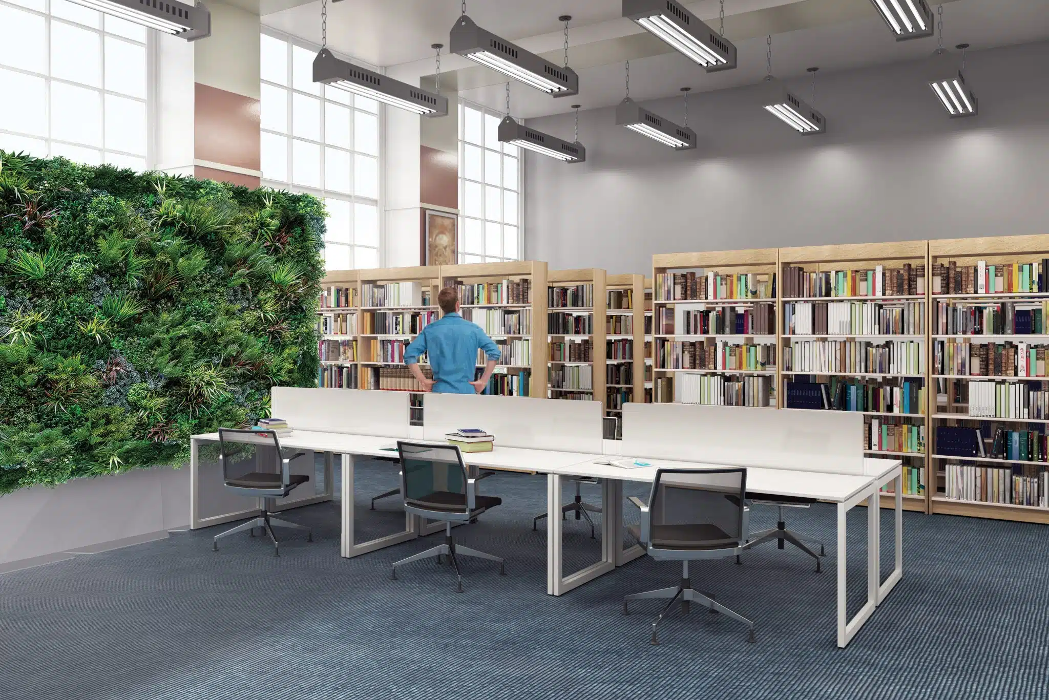 A modern library features wooden bookshelves filled with books, while Modular Green Wall Partitions on the left bring nature indoors. A long white table with chairs in the center anchors the space, where a person browses near the shelves. Large windows flood the area with natural light.
