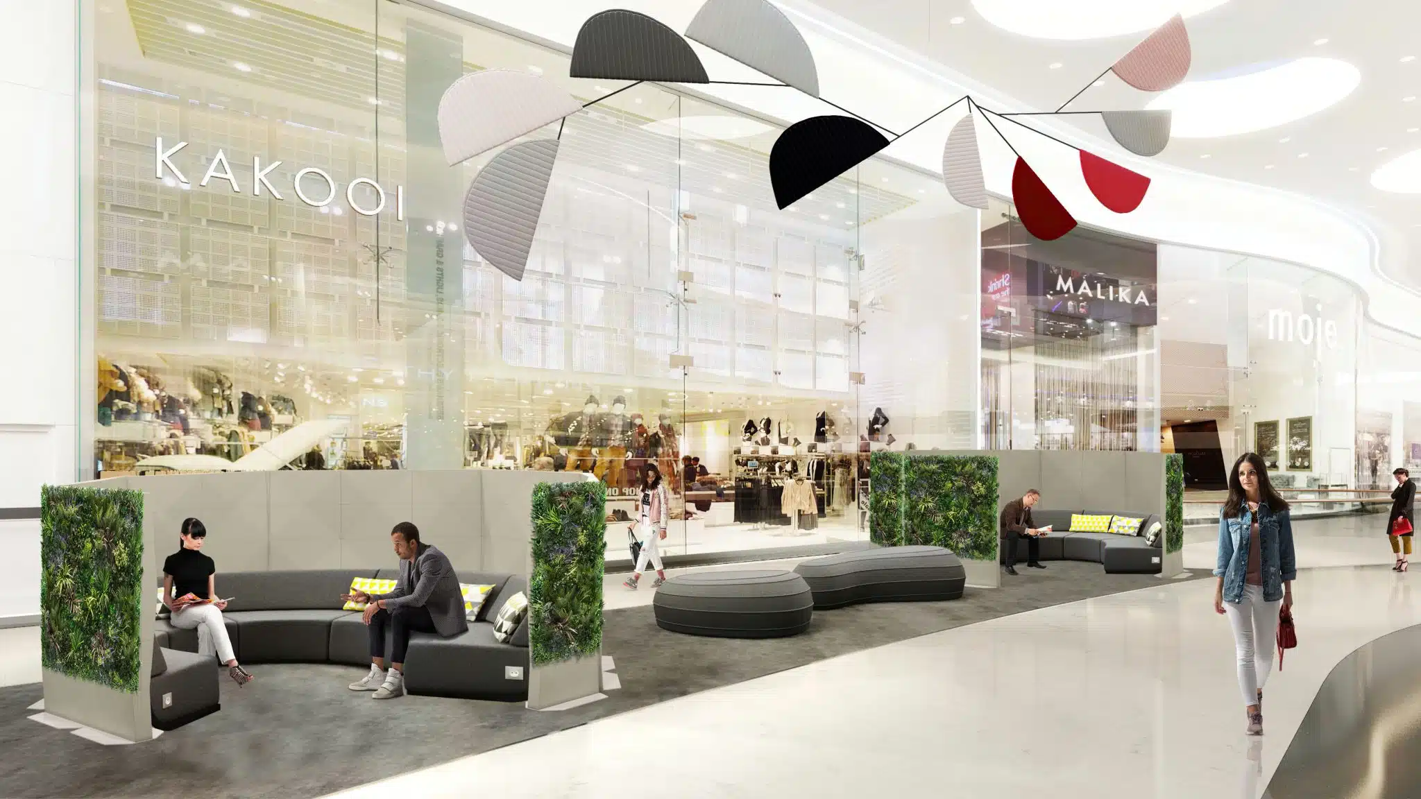 The modern shopping mall interior boasts curved benches and greenery panels, enhanced by Modular Green Wall Partitions. Shoppers walk and relax under a large decorative mobile, with retail stores in the background, including one featuring the Kakoo sign.