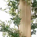 The Extendable Artificial Trailing Foliage features lush green leaves, small white flowers, and delicate brown stems that intertwine along a vertical wooden board, creating a vibrant natural scene against a light background.