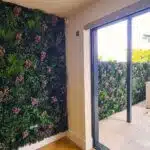 The indoor room transforms with the Spring Pink Colour Box, featuring lush green leaves and clusters of pink flowers. A glass door leads to a plant-themed patio, while light wooden flooring adds warmth.