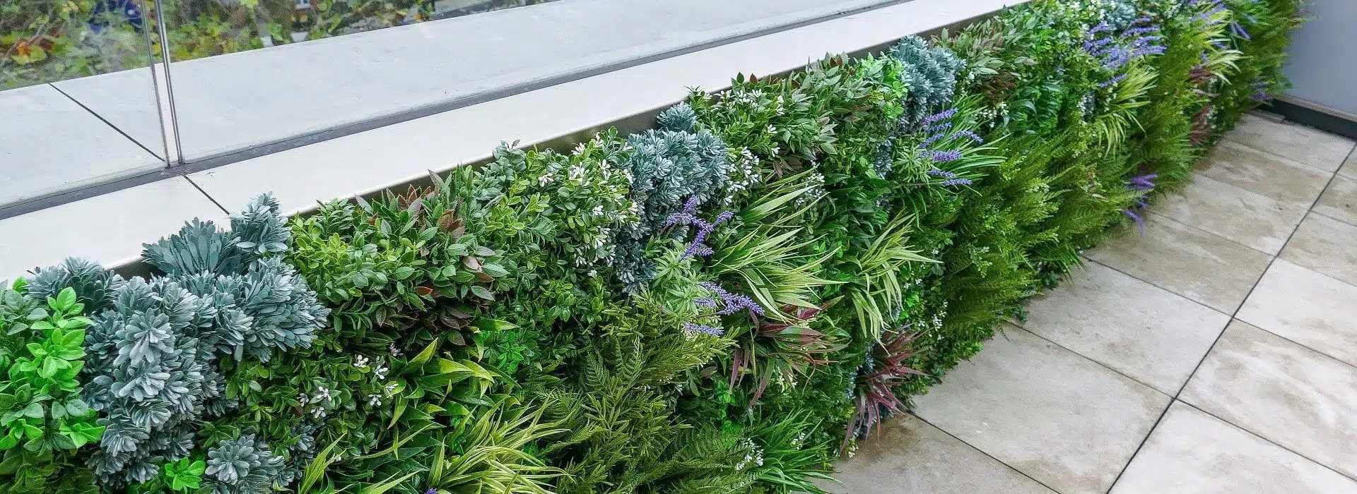 A lush vertical garden with green and purple plants enhances the balcony, acting as a vibrant privacy screen along the metal edge beside a smooth, gray tiled floor. This greenery offers a natural contrast to the sleek, modern setting.
