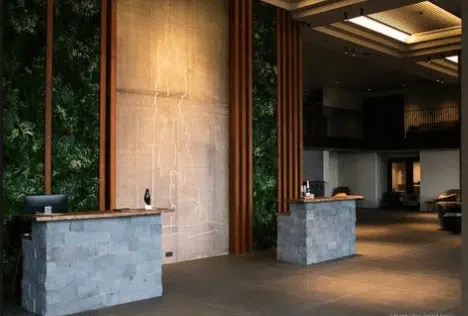 The spacious modern lobby at Hotel Geysir in Iceland features two stone reception desks and vertical wooden slats framing a tall figures outline on the wall. Green foliage adorns sections of the walls, showcasing stunning artificial living walls in a hospitality setting beneath minimalistic ceiling lights.